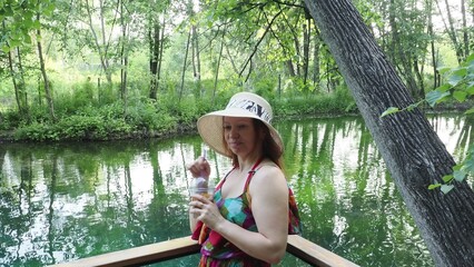 girl in hat on wooden bridge near forest lake, drinking refreshing drink on hot summer day. Vacation. Outdoor recreation. Portrait of happy young . Young woman enjoying a day at the lake.