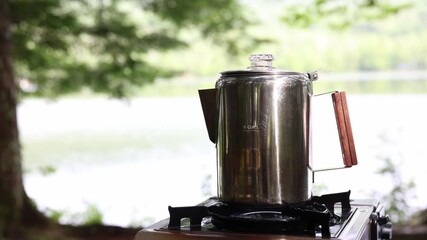 Video of morning coffee brewing and steaming in a percolator on the lakeshore of a campsite
