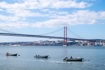 Small fishing boats and a palm tree on the Lisbon waterfront overlooking the Tagus River.