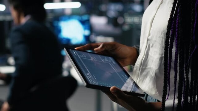 Close up of data center engineer using tablet to review code for automation scripts. Server farm system administrator using device, monitoring error logs for debugging processes, camera A