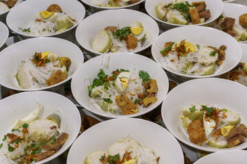 Bowls of soto, a traditional Indonesian dish with rice cake, vermicelli, and egg. Served for a celebration or gathering.