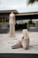 Naklejka premium Elegant beige wedding shoes with crystal details. A beautiful bridal gown stands blurred in the background. Perfect for luxury wedding concepts.