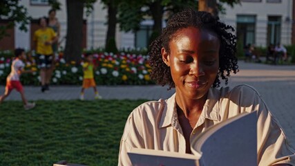 A woman reads a book outdoors in a park, with a low-angle shot capturing the sunlight on her face. The scene feels like a video moment of tranquility.
