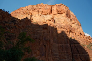 Obraz premium Huge red cliff partially shadowed and partially basked in sunlight with blue skies at zion national park utah in summer time
