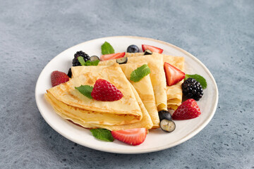 Thin crepes with fresh berries on a blue background. Breakfast. Dessert.