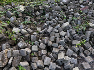 Pile of left over pavers, flooring or concrete block paving, cube shape, with green vines