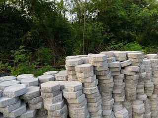 Pile of hexagonal pavers, flooring or concrete block paving, side view, on the edge of green trees