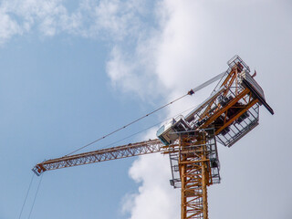 Yellow luffing-jib tower construction crane with white cab against a blue sky and clouds