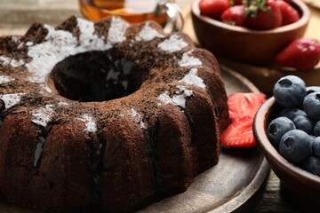 Tasty chocolate bundt cake with glaze, tea and berries on wooden table, closeup