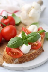 Tasty sandwich with mozzarella cheese, tomatoes and basil on light table, closeup