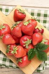 Delicious ripe strawberries and green leaves on wooden table, top view