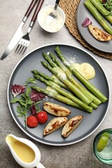 Tasty cooked asparagus served with baked potatoes, tomatoes and sauce on grey table, flat lay