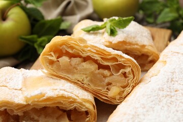 Tasty apple strudels with powdered sugar, mint and fruits on table, closeup