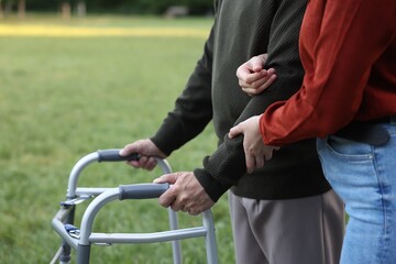Caregiver supporting elderly man who using walking frame outdoors, closeup