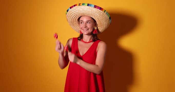 Happy woman in sombrero hat playing maracas on yellow background