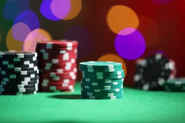 Casino chips on green table against blurred lights, closeup