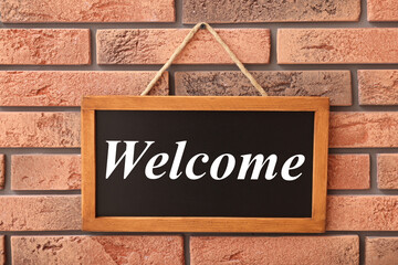 Small chalkboard with word Welcome hanging on brick wall