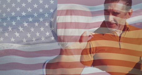 Mother touching adult son shoulder while son holding dark bottle on sandy beach, with flag overlay