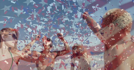 Celebrating 6 friends in swimwear and sunglasses raising arms on beach with fluttering confetti