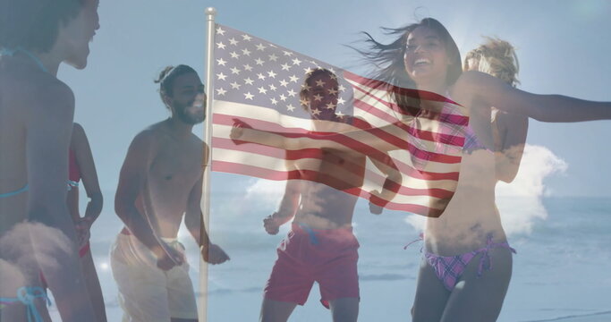 Dancing group of seven friends jumping on sandy beach shoreline, with American flag billowing