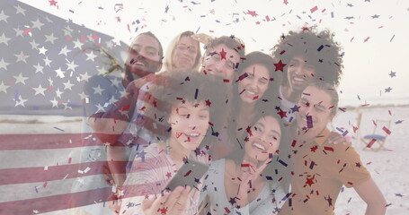 Smiling friends in casual wear at beach, holding smartphone with confetti and American flag overlay