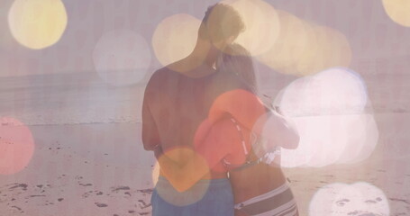 Embracing couple wearing swim trunks, bikini on sandy shore at sunset, holding red inflatable ring