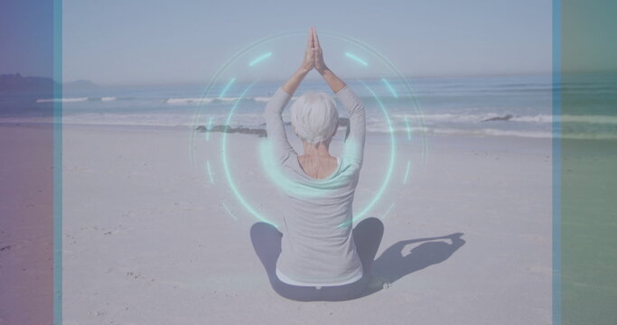 Practicing senior woman raising arms in prayer on sandy beach, with digital holographic overlay