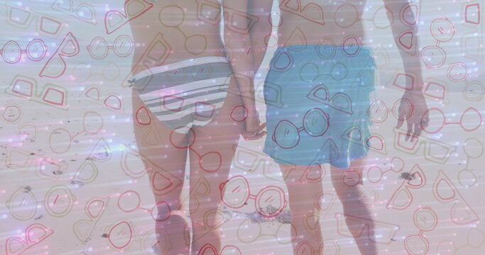 Walking couple holding hands along beach shoreline, with striped bikini bottom and teal swim trunks