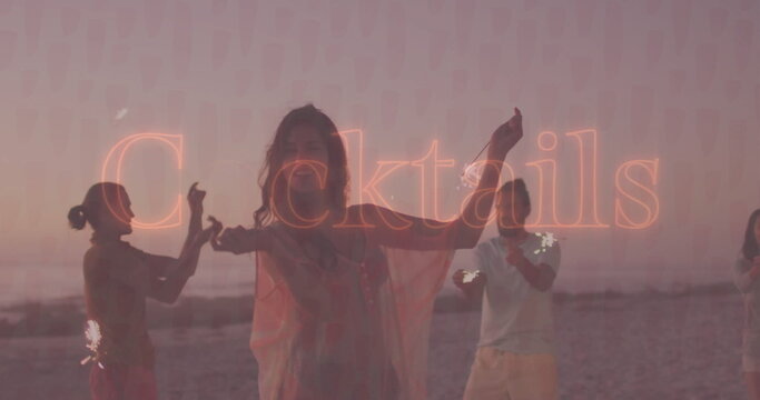 Group of four friends holding lit sparklers on beach at sunset, with neon ‘Cocktails' overlay