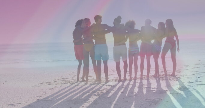 Standing group of eight friends linking arms on sandy beach facing ocean, wearing swimwear - Powered by Adobe