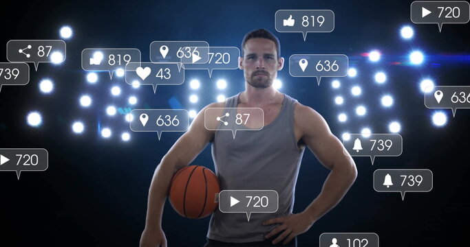 Posing player wearing shirt under court lights, holding orange basketball and social icons floating
