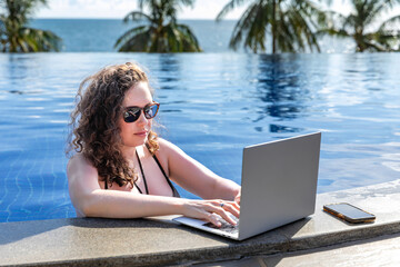Young freelancer traveler woman working remotely on computer at pool in luxury resort during her...