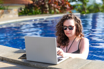 Young freelancer traveler woman working remotely on computer at pool in luxury resort during her...