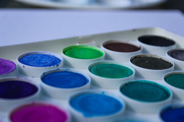 a palette of watercolor paints with various shades of blue, green, purple, brown, and black in...