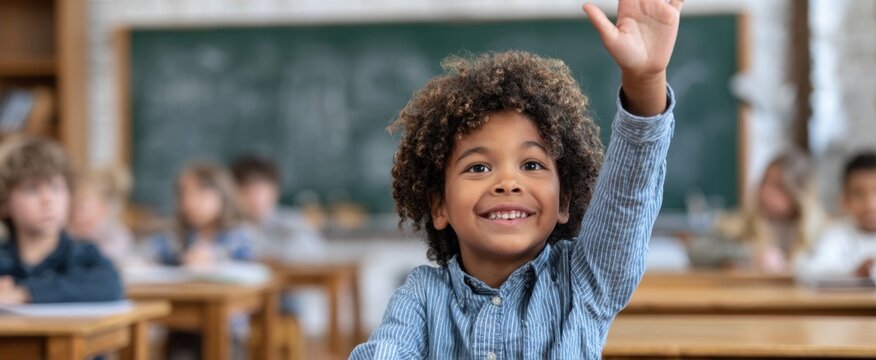 An enthusiastic young student raises his hand in a classroom setting eager to participate in the lesson with a bright smile and positive attitude.