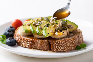 Avocado toast with banana, sunflower seeds, pumpkin seeds, sesame seeds, blueberries, tomatoes and honey, Healthy food