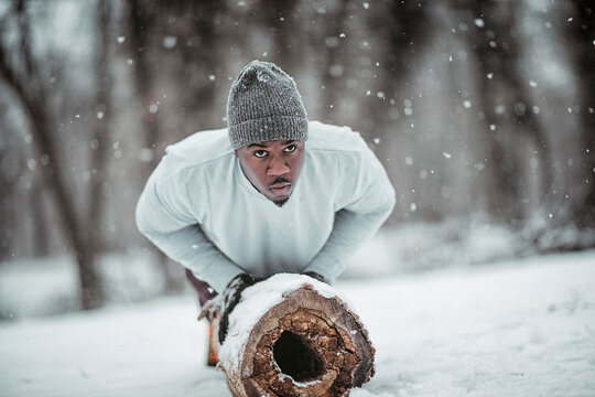 Man doing pushups on log during intense winter workout in snowy forest