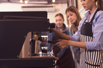 Asian woman entrepreneur making coffee from machine while standing by coworker at cafe. Female barista making coffee in coffee shop counter. Takeaway food. Professional coffee making. Small business.