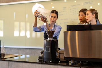 Asian woman entrepreneur making coffee from machine while standing by coworker at cafe. Female barista making coffee in coffee shop counter. Takeaway food. Professional coffee making. Small business.