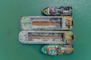 Aerial top-down view of two barges loaded with dredged material and supported by tugboats, floating...