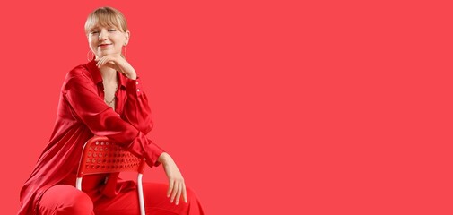 Stylish young woman sitting on chair against red background with space for text