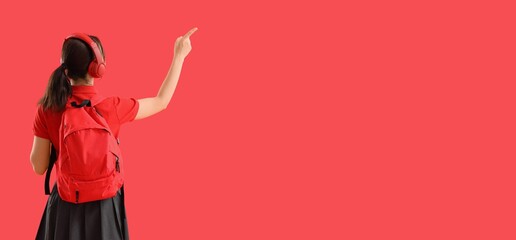 Female student in headphones pointing at something on red background, back view. Banner for design