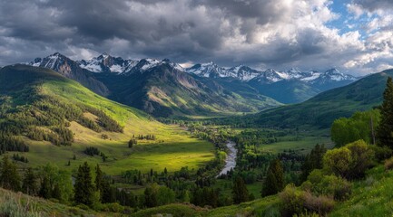 Fototapeta premium Panoramic view of a verdant valley nestled between snow-capped mountains, bathed in sunlight, with a river winding through the meadows