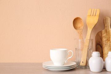 Kitchen utensils, cup and saucers on wooden table near beige wall