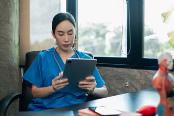 A focused healthcare worker in blue scrubs uses a tablet in a contemporary office, highlighting...