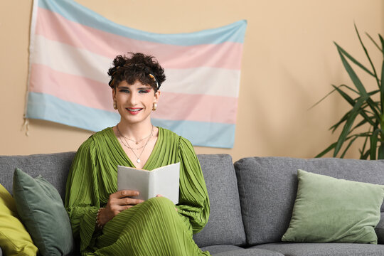 Young transgender woman reading book on sofa at home