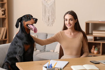 Cute Doberman dog and beautiful young happy woman with notebooks sitting on workplace at home