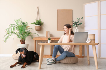 Cute Doberman dog and beautiful young happy woman with laptop at workplace at home