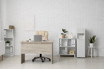 Interior of light office with modern water cooler, workspace and shelving unit
