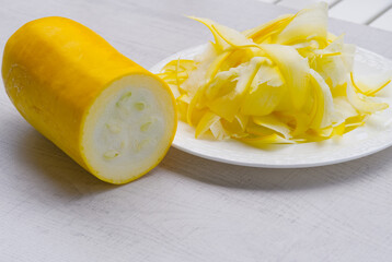 Sliced yellow zucchini on white plate on wood background.